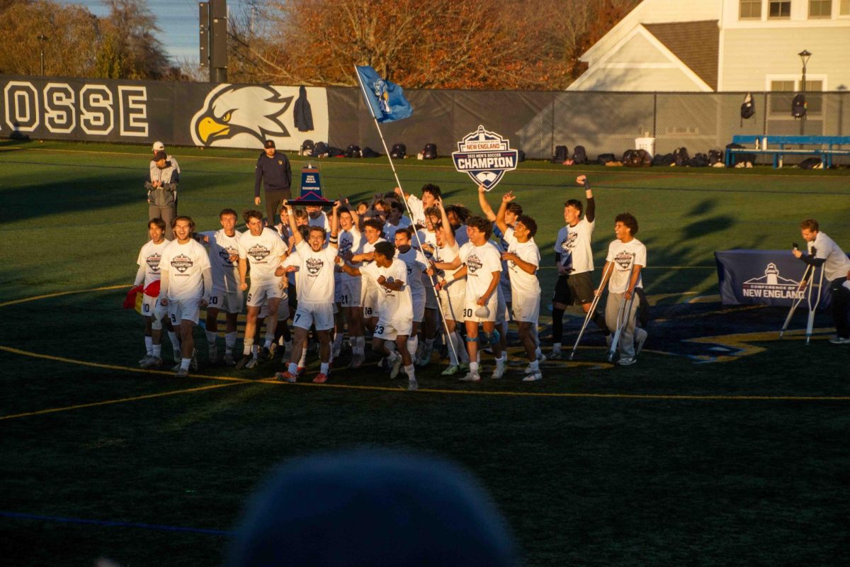 RWU Men's Soccer team celebrating with CNE championship win with their trophy and flag.